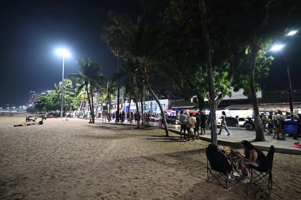 Nighttime beach promenade lined with palm trees and streetlights, people strolling along the sand