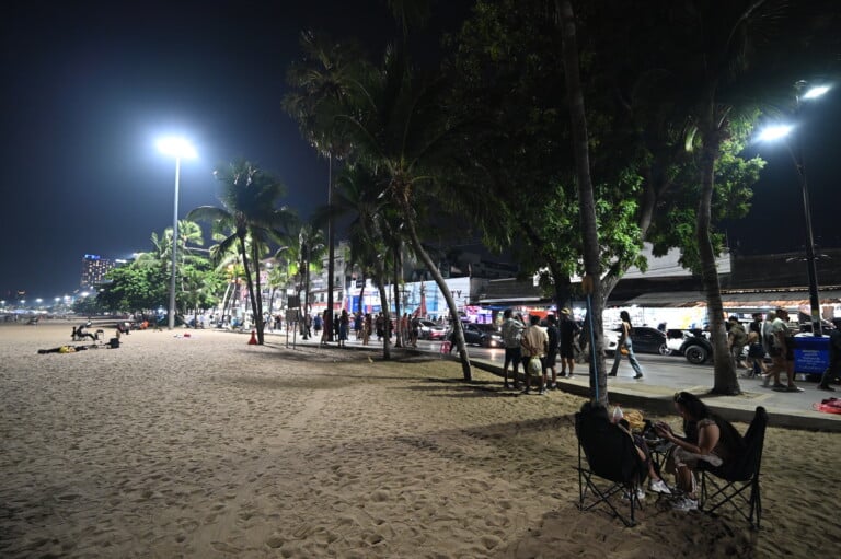 Nighttime beach promenade lined with palm trees and streetlights, people strolling along the sand