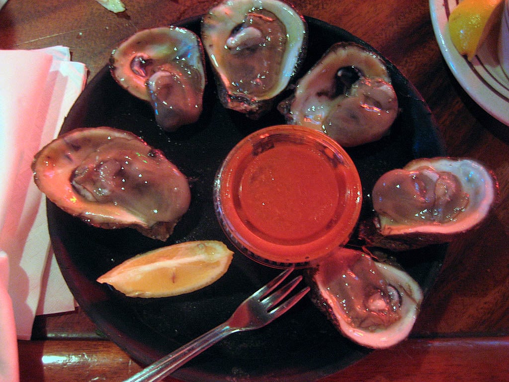 A dozen raw oysters on the half shell served on ice with lemon and sauce