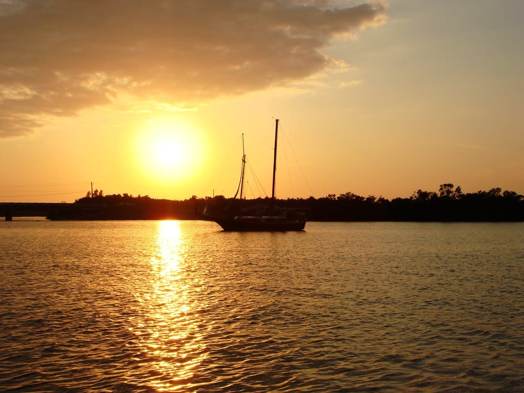 Sailboat silhouetted against a golden sunset on Estero Bay, Florida