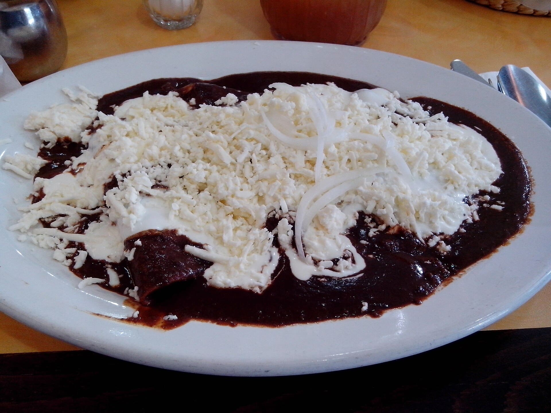 A plate of enchiladas in dark mole poblano sauce topped with crumbled cheese