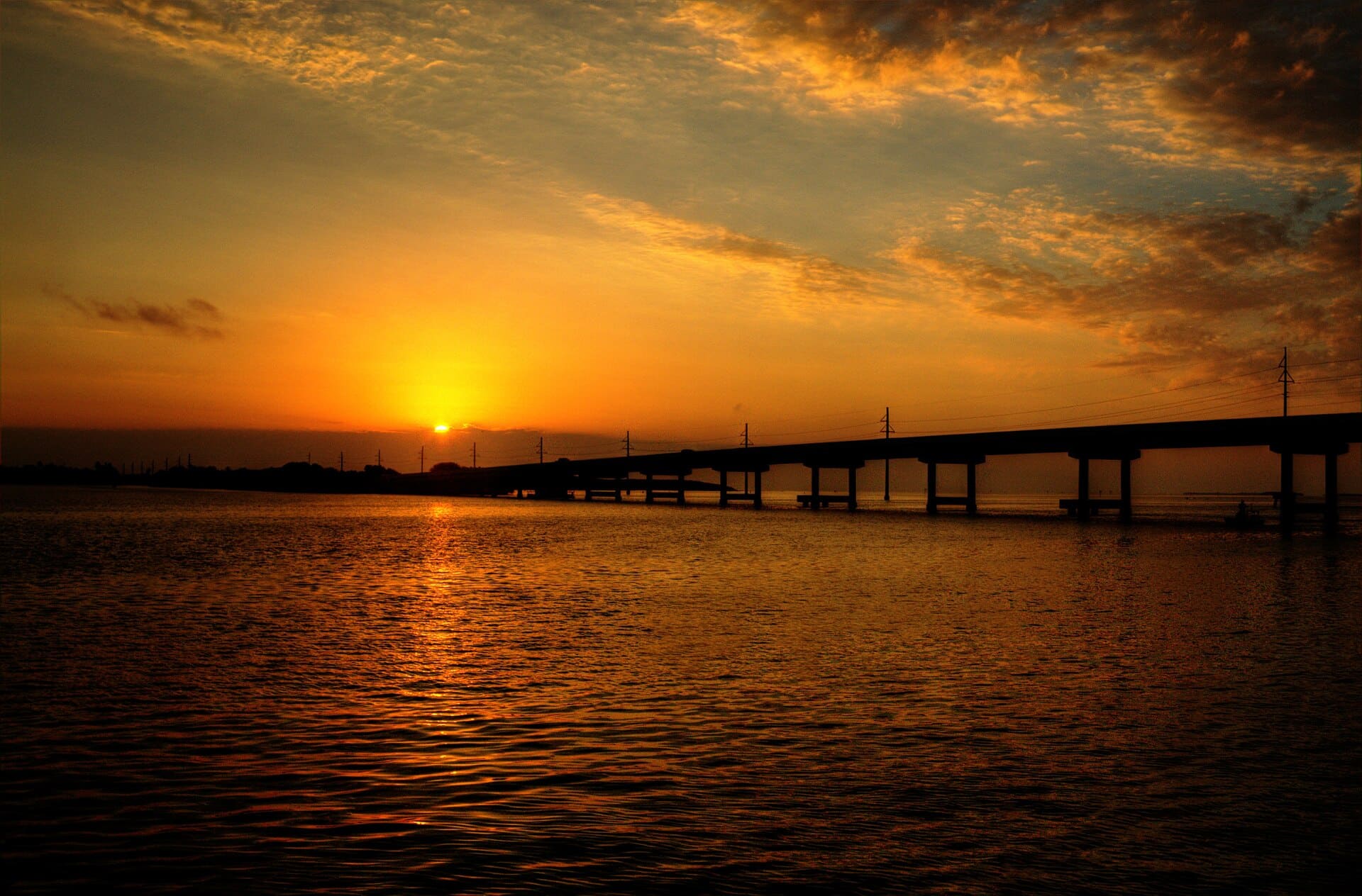 Golden sunset over calm bay water with a bridge in the distance in Southwest Florida