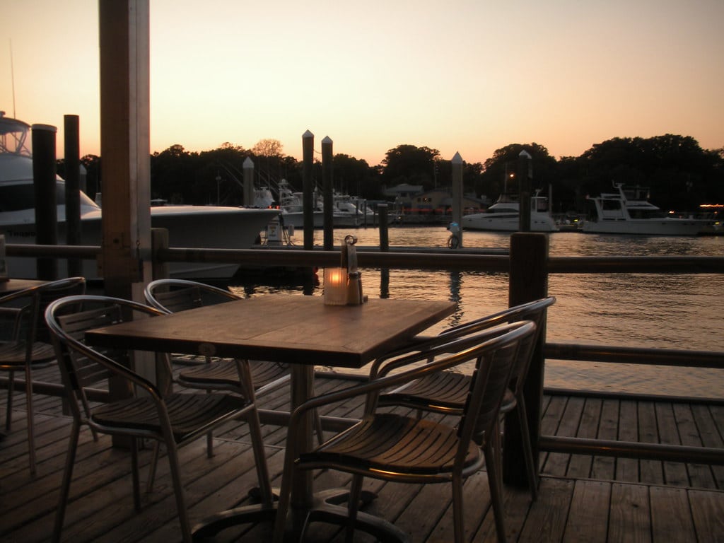Waterfront restaurant deck tables overlooking boats and the bay at sunset
