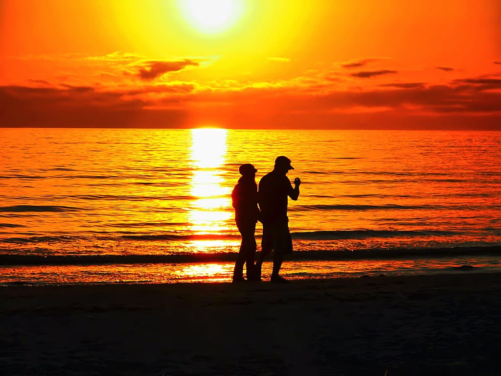 Couple silhouetted against a fiery orange sunset on Fort Myers Beach