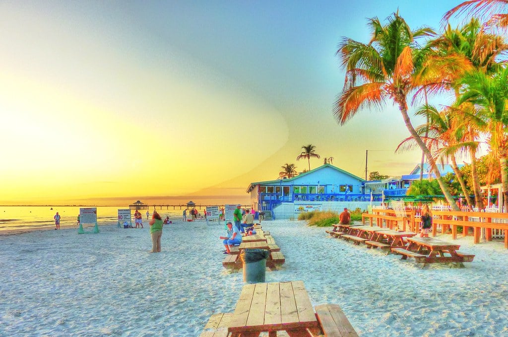 Beachfront bar with picnic tables and palm trees on the sand at Fort Myers Beach at sunset