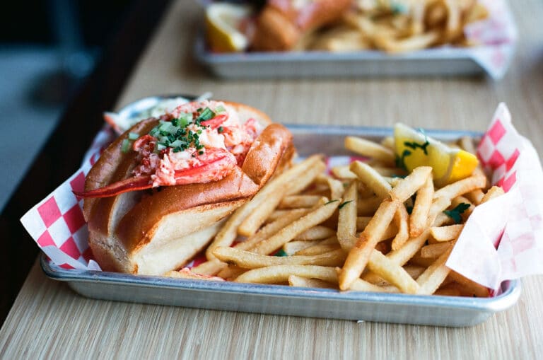 A buttered lobster roll served with fries in a paper-lined basket