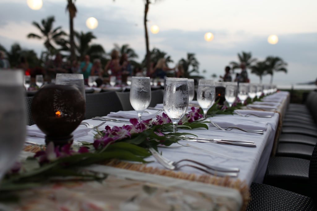 A long dinner table set with glassware and flowers on the beach at sunset
