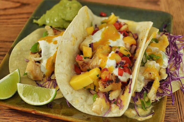 Two fish tacos topped with slaw and mango salsa on a plate