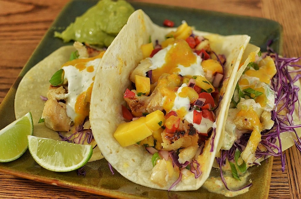 Two fish tacos topped with slaw and mango salsa on a plate
